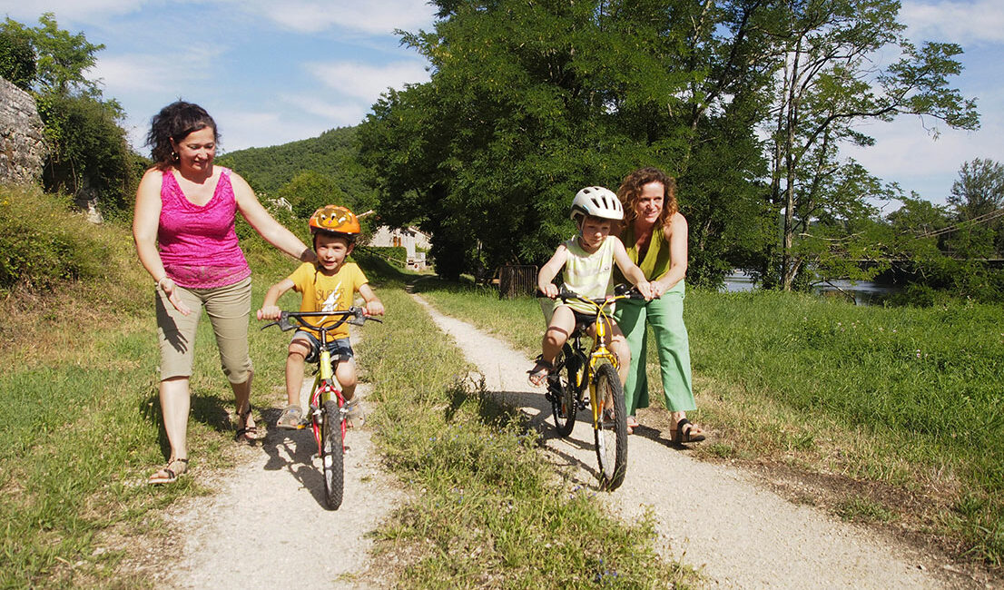 deux mamans apprennent à deux petits garçons à faire du vélos sur le chemin de halage, près de la rivière