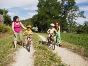 deux mamans apprennent à deux petits garçons à faire du vélos sur le chemin de halage, près de la rivière