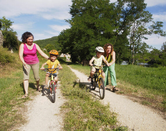 deux mamans apprennent à deux petits garçons à faire du vélos sur le chemin de halage, près de la rivière